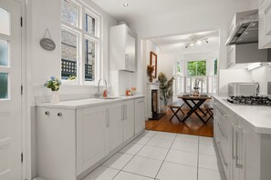 Cozinha moderna com armários brancos, área de refeições com mesa e cadeiras, e vista para o exterior através de grandes janelas.