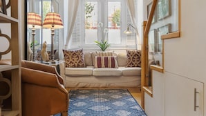 A cozy living room with a sofa, patterned cushions, a blue patterned rug, and a wooden chair. - Stylish 1-bed Flat in the Heart of Kensington (London)
