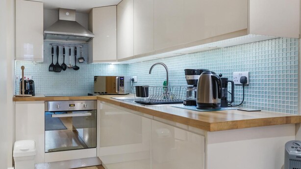 A modern kitchen with white cabinets, a stainless steel oven, a coffee maker, and a toaster. - Stylish 1-bed Flat in the Heart of Kensington (London)