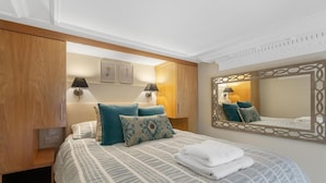 A neatly arranged hotel room with a bed, bedside lamps, a mirror, and a wooden wardrobe. - Stylish 1-bed Flat in the Heart of Kensington (London)