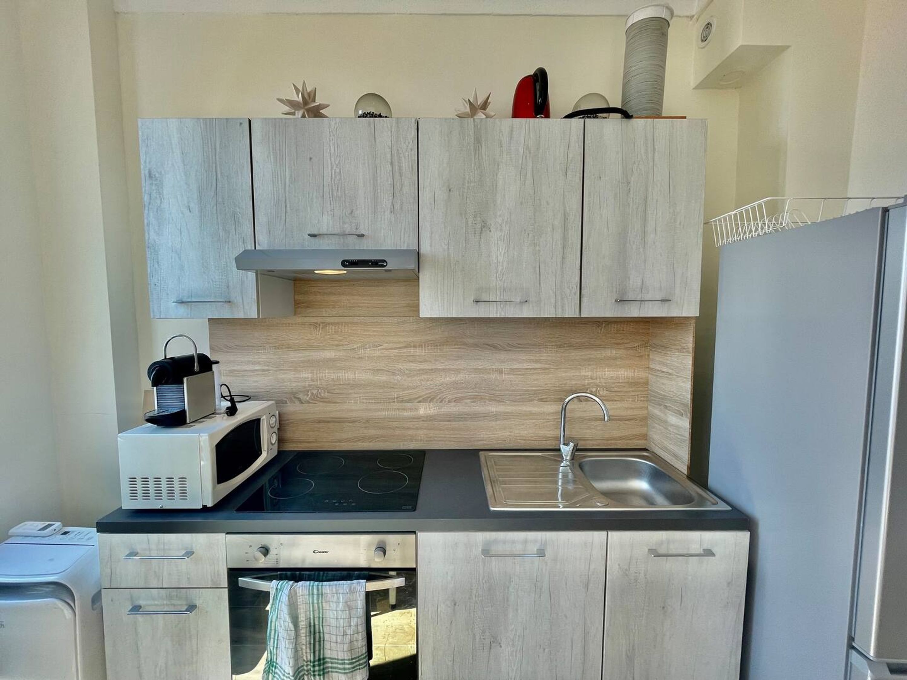 A compact kitchen with light wood cabinets, a stainless steel sink, a microwave, and an oven.