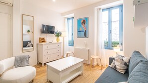 Ein modernes Wohnzimmer mit einer Couch, einem Couchtisch, einem Fernseher, einem Schreibtisch und einem Fenster mit Vorhängen.