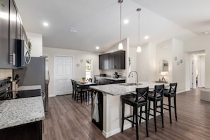 A modern kitchen with granite countertops, dark cabinetry, a central island with bar stools, and pendant lighting. - Villa Bennett NEW 4-bedroom With Pool spa (Inverness)