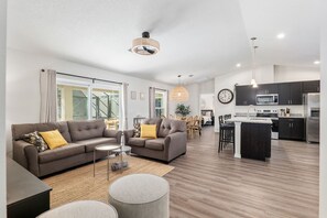 A modern living room with a sofa, coffee table, and a dining area with chairs. - Villa Bennett NEW 4-bedroom With Pool spa (Inverness)