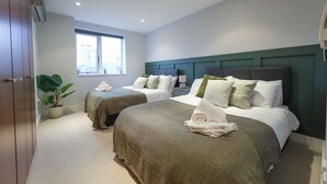 Una habitación de hotel con dos camas, un ventanal grande, una planta en maceta y un armario.