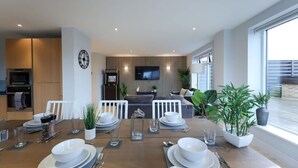 Un comedor moderno con una mesa de madera preparada para cuatro personas, un televisor montado en la pared y vistas al exterior.