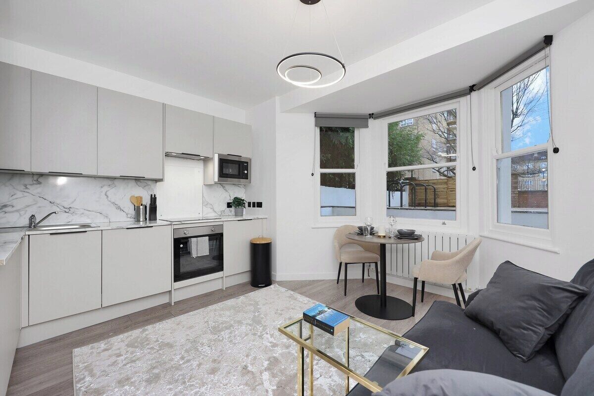 A modern kitchen with white cabinets, a marble countertop, and a dining area with a table and chairs.