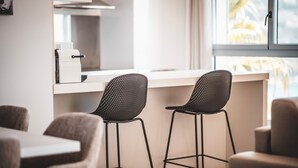 Een moderne keuken met twee zwarte stoelen van mesh, een wit aanrecht en een raam met uitzicht op palmbomen.