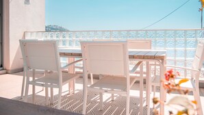 Een balkon met witte stoelen en een tafel, een vloer met patroon en een heldere lucht.