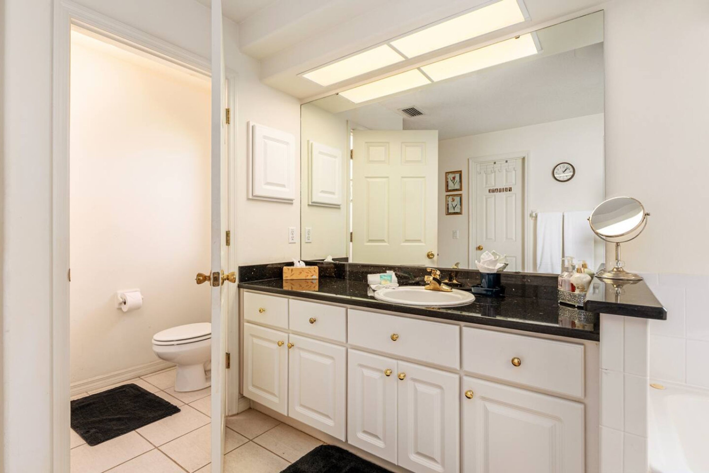 Une salle de bain avec des toilettes blanches, un lavabo avec un miroir et un comptoir noir.