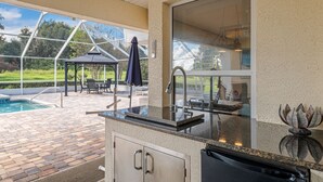 Een buitenkeuken met een zwembad, terrasmeubilair en een pergola.
