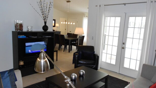 A living room with a TV, a coffee table, a sofa, and a dining area in the background. - Villa Luva Spectacular Villa With Pool (Hernando)