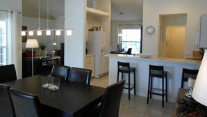 A modern kitchen with white cabinets, a dining area with a black table and chairs, and a visible clock on the wall. - Villa Luva Spectacular Villa With Pool (Hernando)