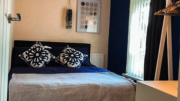 A bedroom with a bed, a hanging plant, a framed picture, and a window with curtains.