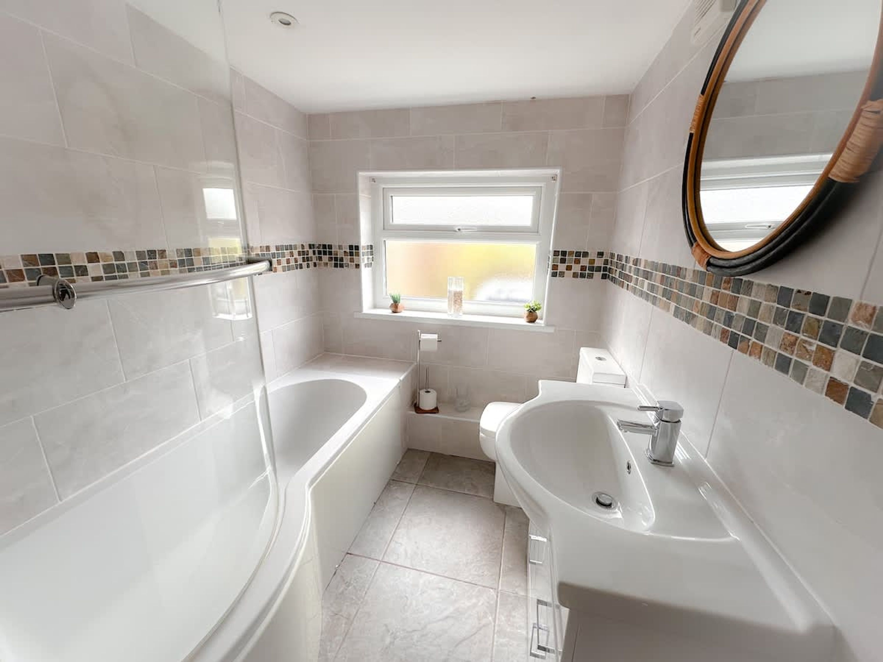 Un baño moderno con bañera, lavamanos e inodoro. Hay una ventana que ofrece vistas al exterior.