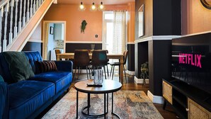 A living room with a blue sofa, a coffee table, a fireplace with a Netflix sign, and a staircase.