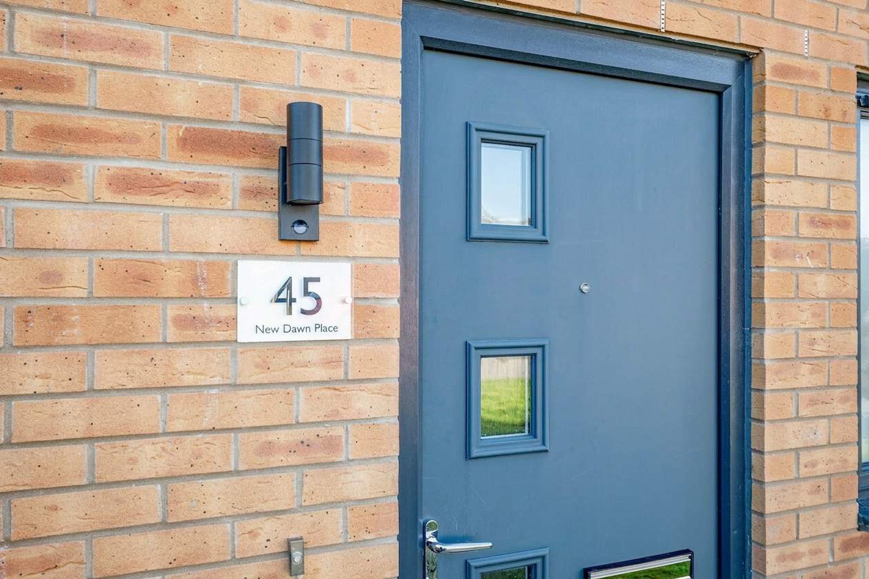 A blue door with a number '45' and a sign 'New Dawn Place' on a brick wall.