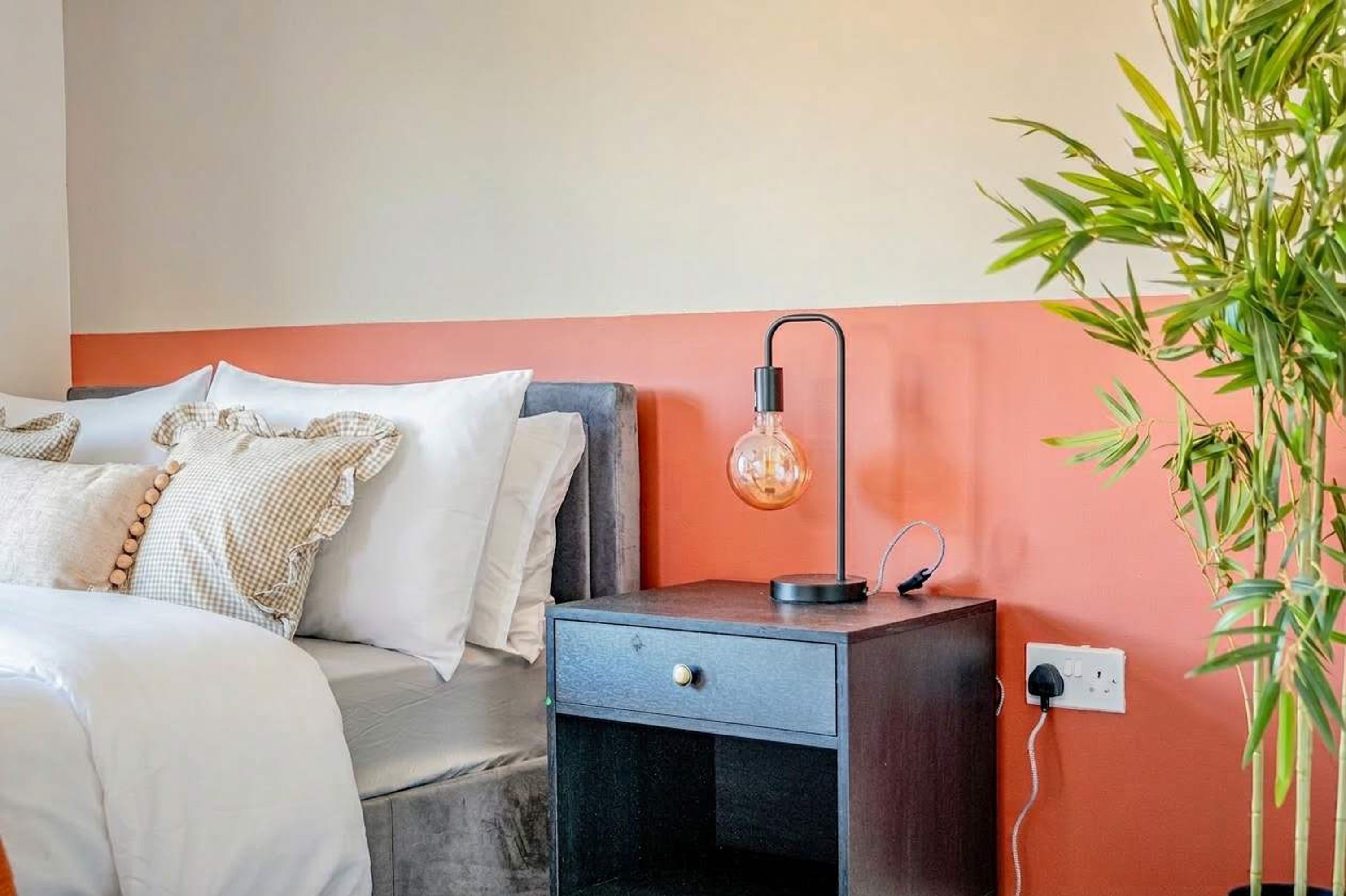 Un dormitorio con una cama, mesita de noche, lámpara y una planta en maceta.