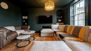 A living room with a dark green wall, a large window, a fireplace, a television, and a chandelier. - Stunning Bath Home Sleeps 12 Ideal for Hen Stags (Bath)