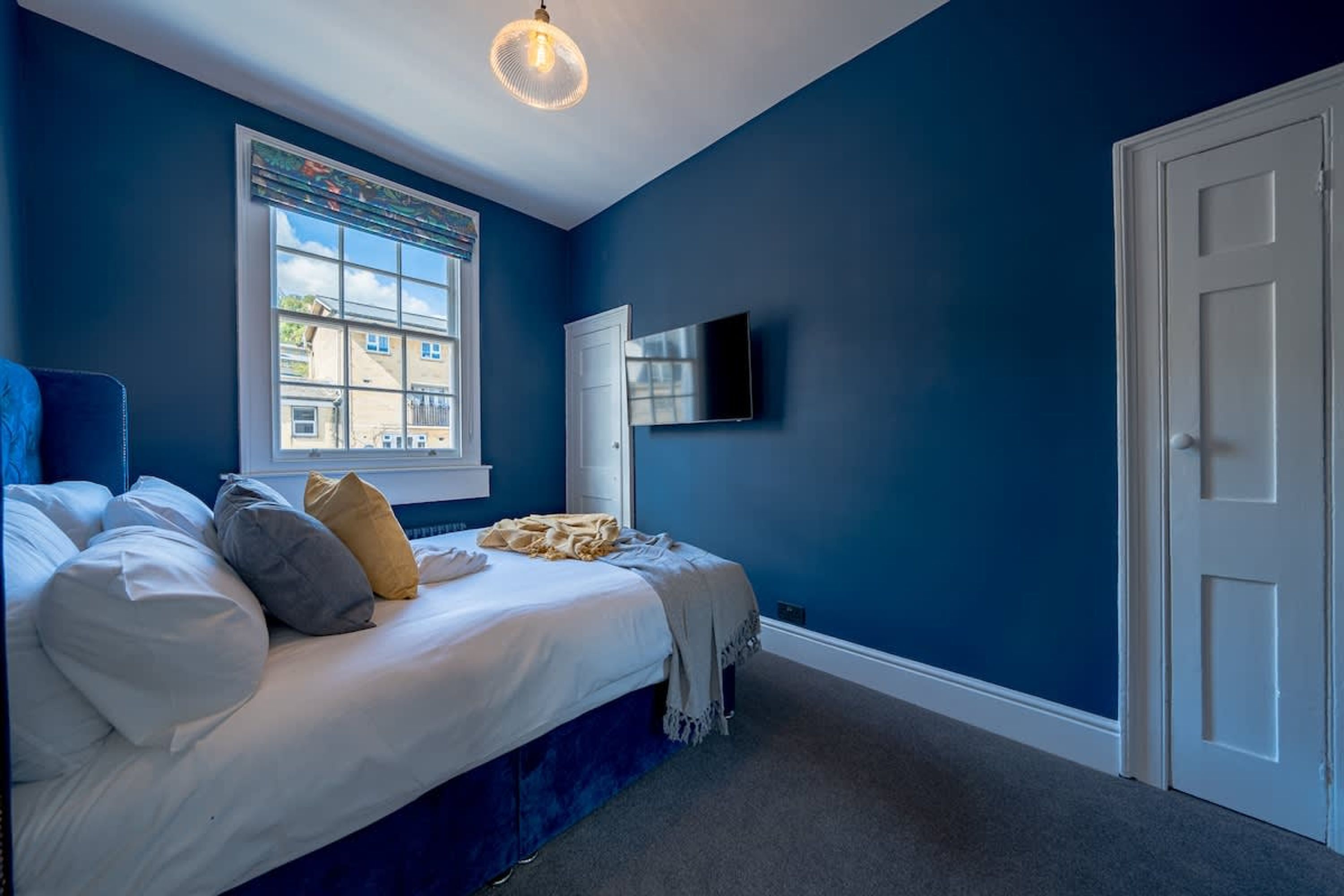A bedroom with a bed, a window with blinds, a television, and a door.