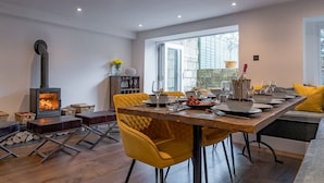A dining area with a table set for four, yellow chairs, a fireplace, and a large window. - Stunning Bath Home Sleeps 12 Ideal for Hen Stags (Bath)