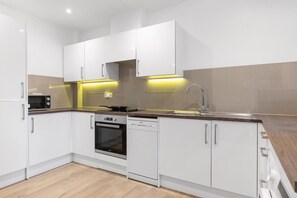 A modern kitchen with white cabinets, a built-in oven, a dishwasher, and a stainless steel sink. - Garden Flat in Central London (London)