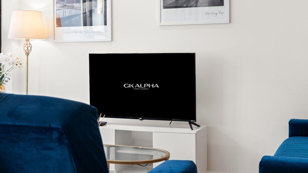 A modern living room with a flat-screen TV, blue upholstered chairs, a white console, and framed pictures on the wall. - Perfect Booking 3 Bed Home In Kensal Green (London)
