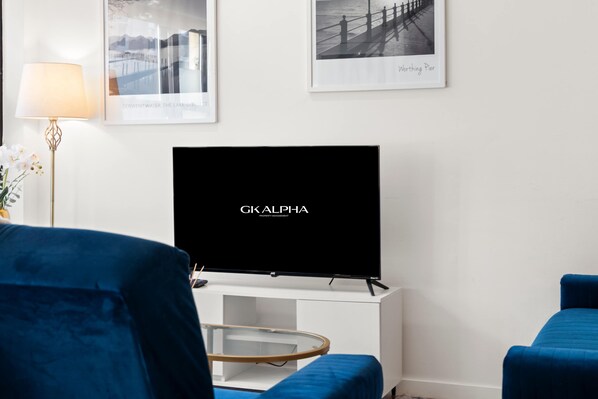 A modern living room with a flat-screen TV, blue upholstered chairs, a white console, and framed pictures on the wall. - Perfect Booking 3 Bed Home In Kensal Green (London)