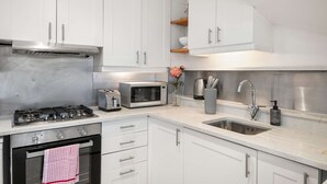 A modern kitchen with white cabinets, stainless steel appliances, a gas stove, a microwave, and a sink. - Perfect Booking 3 Bed Home In Kensal Green (London)
