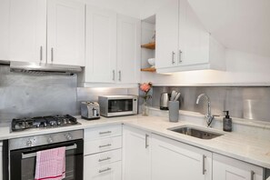 A modern kitchen with white cabinets, stainless steel appliances, a gas stove, a microwave, and a sink. - Perfect Booking 3 Bed Home In Kensal Green (London)