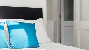 A bed with a black headboard, white bedding, and two pillows, one blue and one white. - Perfect Booking 3 Bed Home In Kensal Green (London)