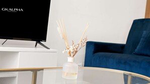 A modern living room with a glass coffee table, a vase with dried flowers, a flat-screen TV, and a blue sofa. - Perfect Booking 3 Bed Home In Kensal Green (London)
