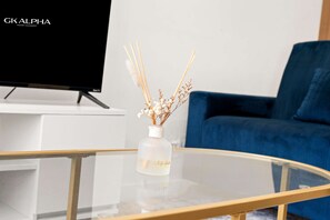 A modern living room with a glass coffee table, a vase with dried flowers, a flat-screen TV, and a blue sofa. - Perfect Booking 3 Bed Home In Kensal Green (London)