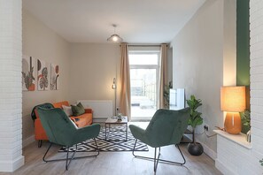 A modern living room with a sofa, two chairs, a coffee table, a lamp, and a view through a window.