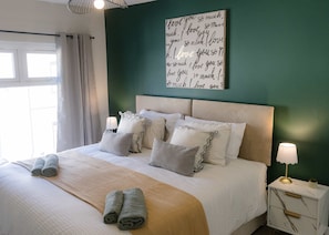 A neatly made bed with pillows, a bedside lamp, and a wall art piece with text.