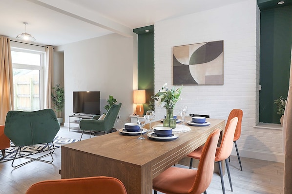 A dining area with a wooden table, orange chairs, a TV, and a potted plant.