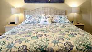 A bedroom with a bed, two bedside lamps, a wall-mounted shark artwork, and a pillow with 'BEACH LIFE' text. - Apartment Live Oak Landing (Inverness)