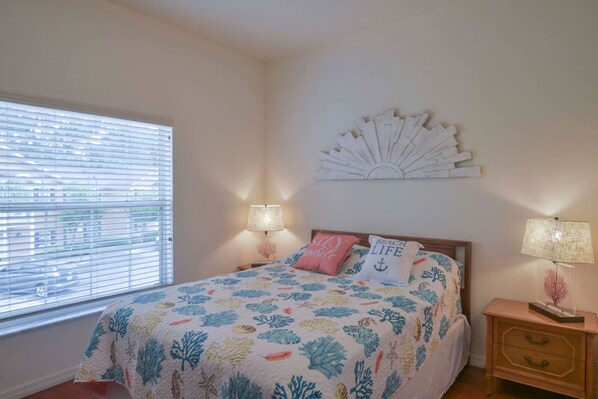 A bedroom with a bed, two bedside lamps, a window with blinds, and a wall decoration.