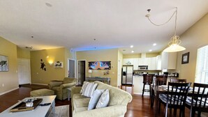 A living room with a sofa, a dining table with chairs, a kitchen area, and a hallway. - Apartment Live Oak Landing (Inverness)