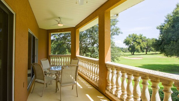 A covered balcony with a table and chairs, a view of a golf course, and a ceiling fan. - Apartment Live Oak Landing (Inverness)