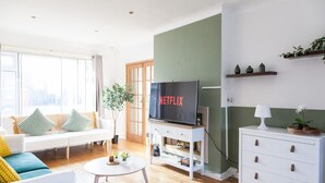 A modern living room with a sofa, a coffee table, a TV on a stand, a small white table, and a cabinet. - Perfect Booking 4 Bed Home Near City Airport (Cheadle)