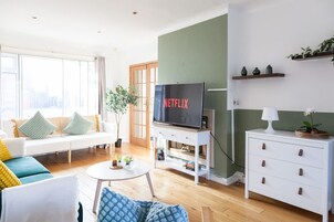 A modern living room with a sofa, a coffee table, a TV on a stand, a small white table, and a cabinet.