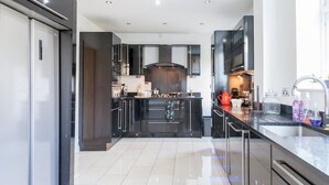 A modern kitchen with dark cabinetry, a central island, and a large window. - Perfect Booking 4 Bed Home Near City Airport (Cheadle)