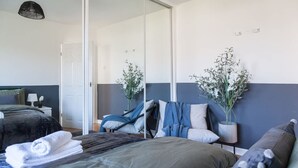 A modern hotel room with a bed, a chair, a mirror, and two potted plants. - Perfect Booking 4 Bed Home Near City Airport (Cheadle)