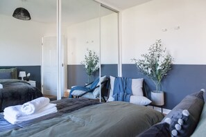 A modern hotel room with a bed, a chair, a mirror, and two potted plants. - Perfect Booking 4 Bed Home Near City Airport (Cheadle)