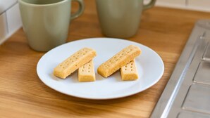 A plate with three rectangular biscuits on a white plate, two green mugs on a wooden surface, and a kitchen counter. - 2 Bedroom SE London Home - Cosy Great Location (London)