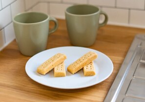 Een bord met drie rechthoekige koekjes, twee groene mokken op een houten oppervlak en een keukentrap.