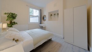A bedroom with a bed, bedside table, lamp, potted plant, window, mirror, and wardrobe. - 2 Bedroom SE London Home - Cosy Great Location (London)