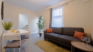 A living room with a sofa, a dining table with chairs, a small table with wine glasses, and a plant. - 2 Bedroom SE London Home - Cosy Great Location (London)