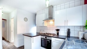 A compact kitchen with white cabinets, a gas stove, an oven, and a stainless steel sink. - Perfect Booking 4 Bed Home in Leytonstone (London)